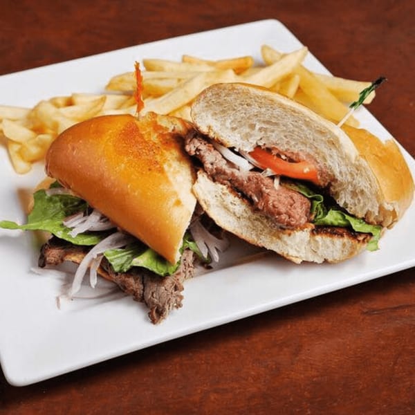 Peruvian steak sandwich with lettuce, onions, and tomatoes, served with a side of french fries.