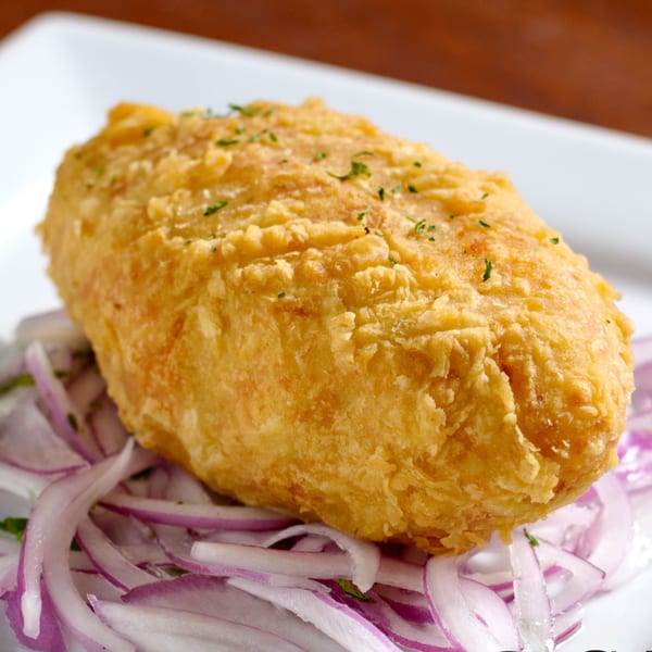 Golden-fried Peruvian papa rellena, a stuffed potato, served on a bed of thinly sliced red onions.