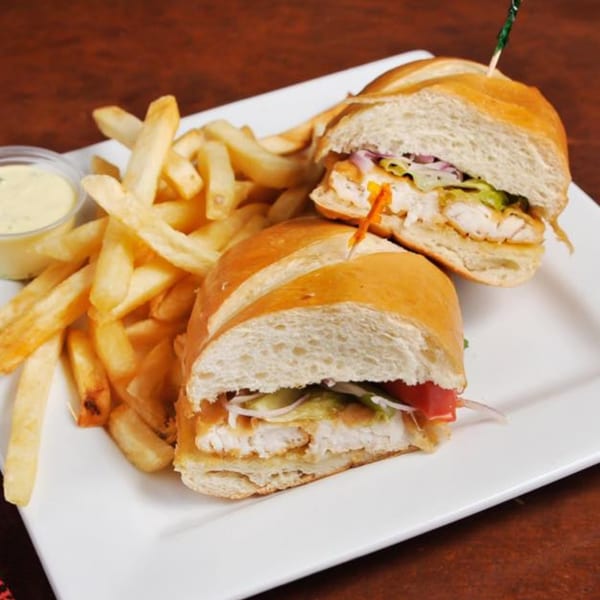 Two halves of a Peruvian fried fish sandwich with fries and dipping sauce on a white plate.