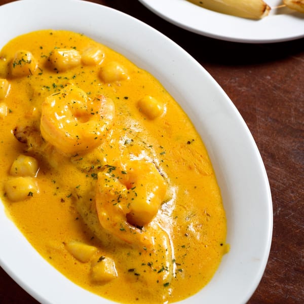 Peruvian aji de gallina, a creamy yellow stew with shrimp and potatoes, garnished with parsley.