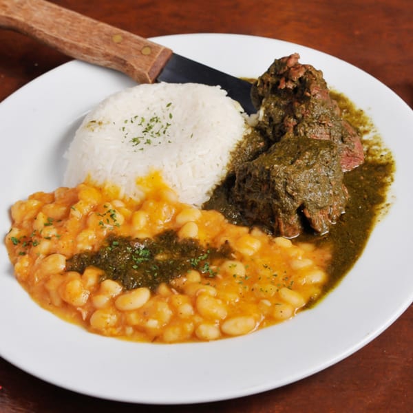 Peruvian seco de res with white rice and canary beans, garnished with parsley on a white plate.