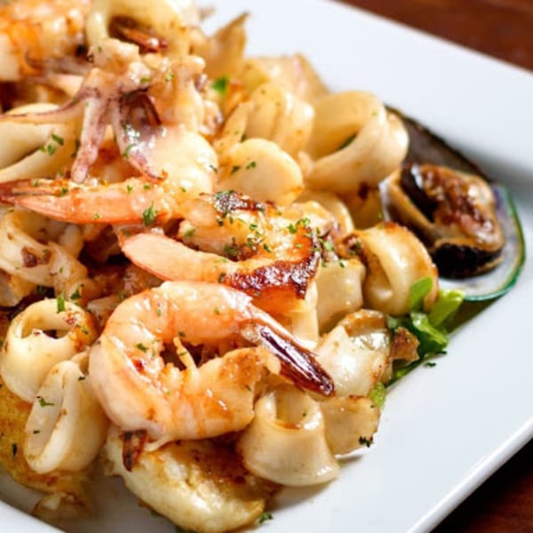 Peruvian seafood dish with shrimp, calamari, and mussels, garnished with parsley on a white plate.