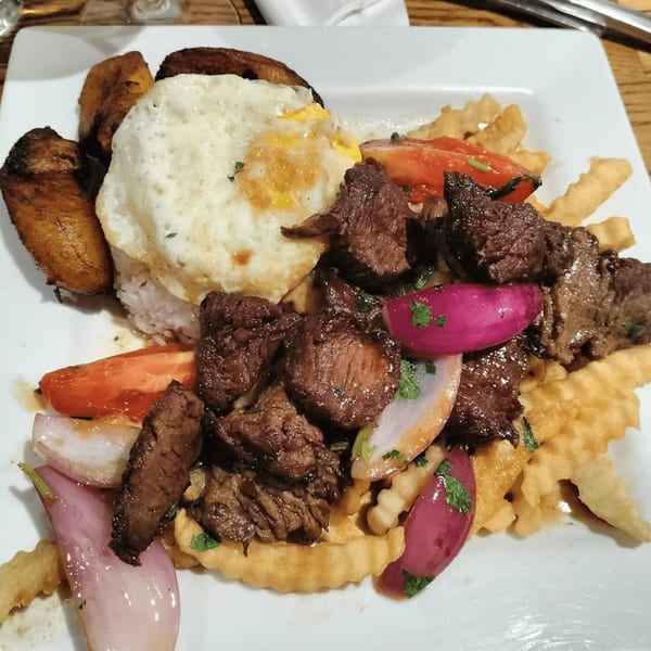 Peruvian Lomo Saltado with steak, red onions, tomatoes, fries, fried plantains, and a fried egg.
